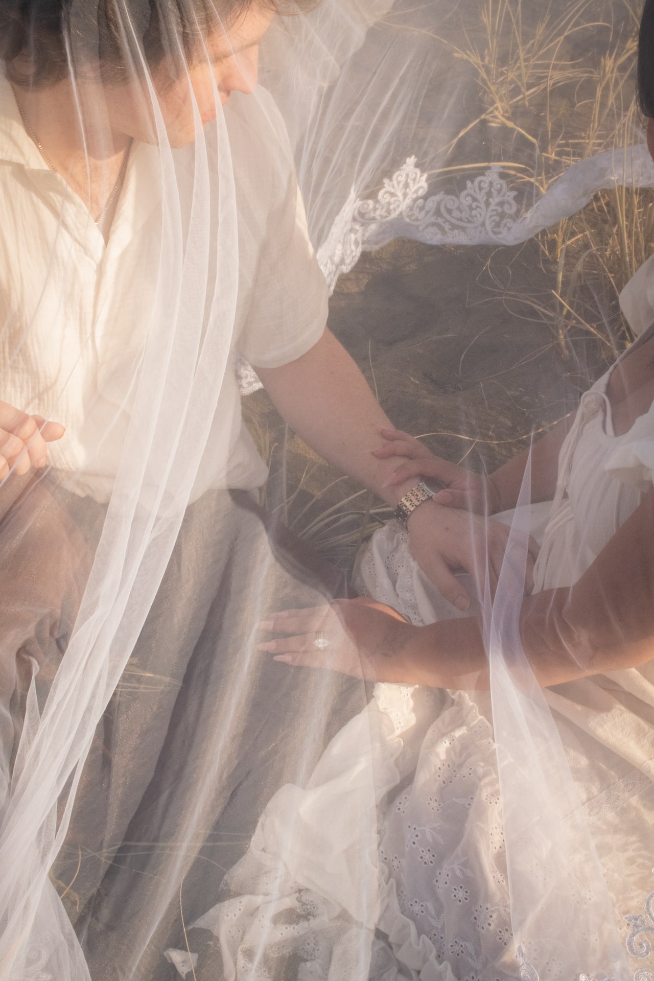 Close engagement portrait of hands and lace detail seen through a sheer veil in warm light