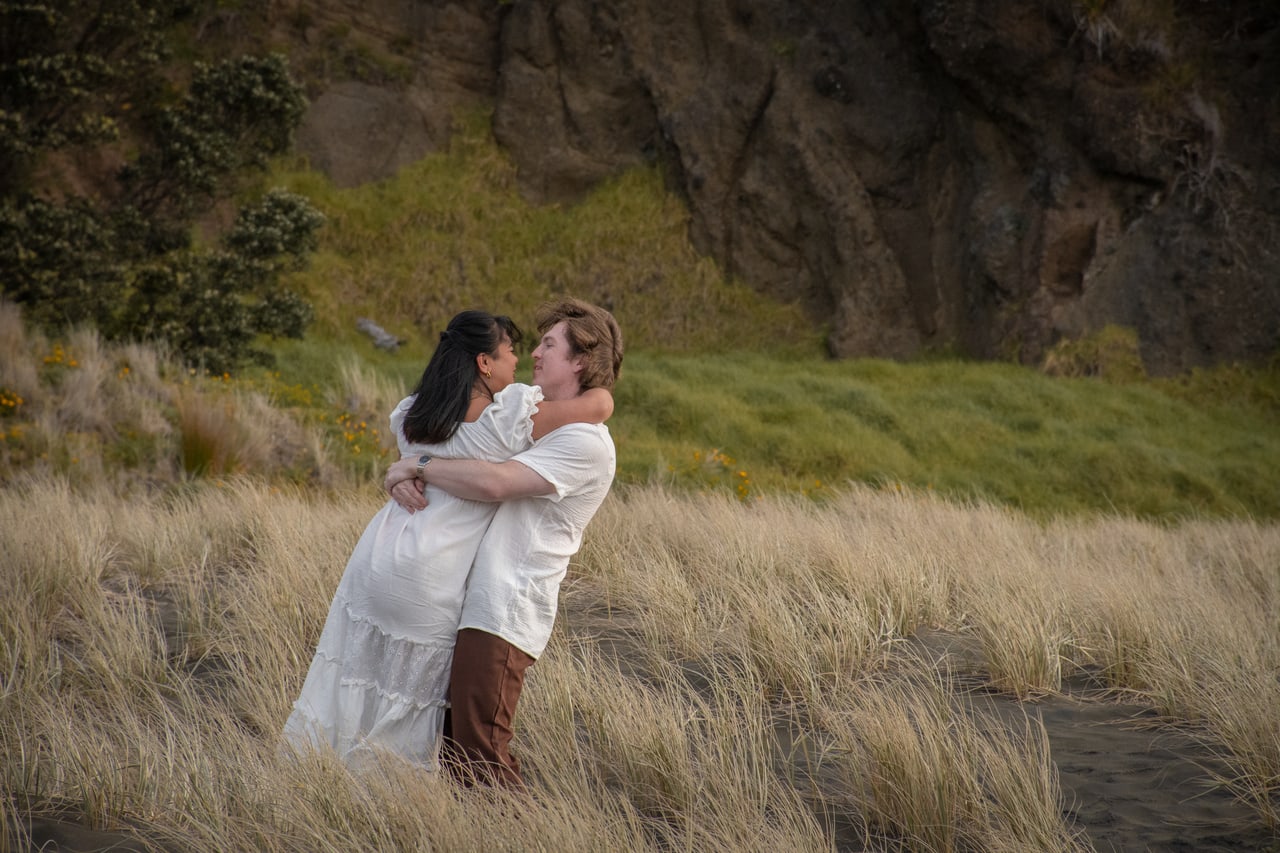 Couple embracing in tall dune grass beneath a coastal cliff