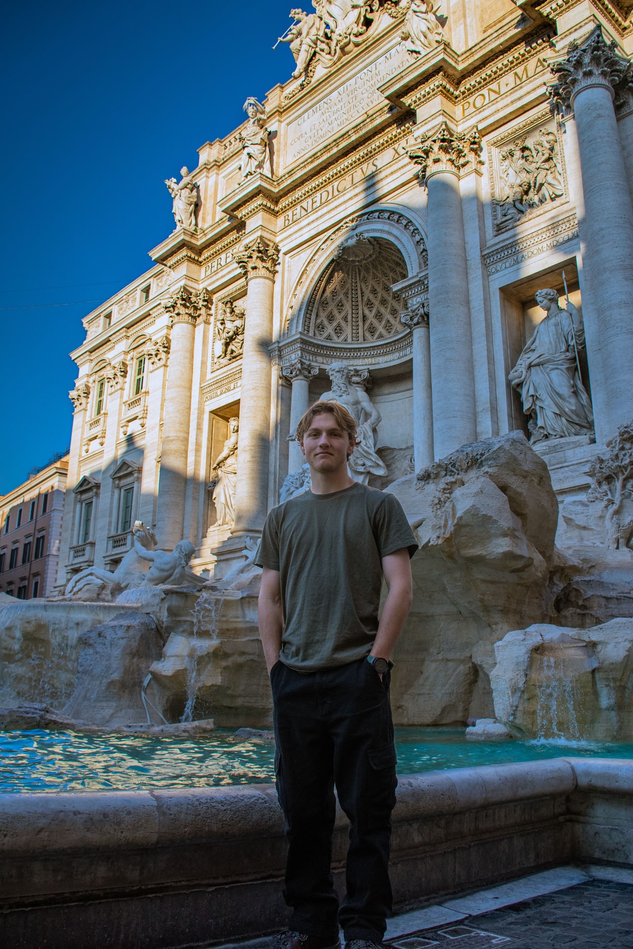 Portrait of a person standing before the Trevi Fountain architecture and turquoise water in Rome