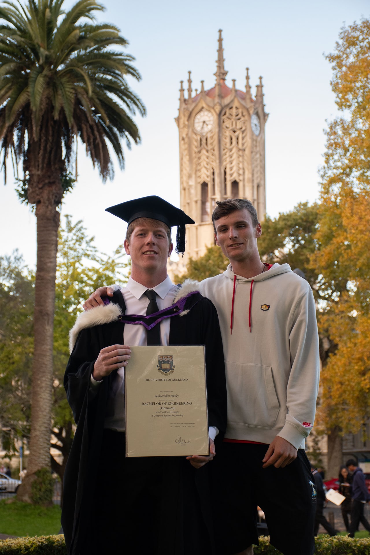 Graduate holding a University of Auckland engineering degree in front of the ClockTower