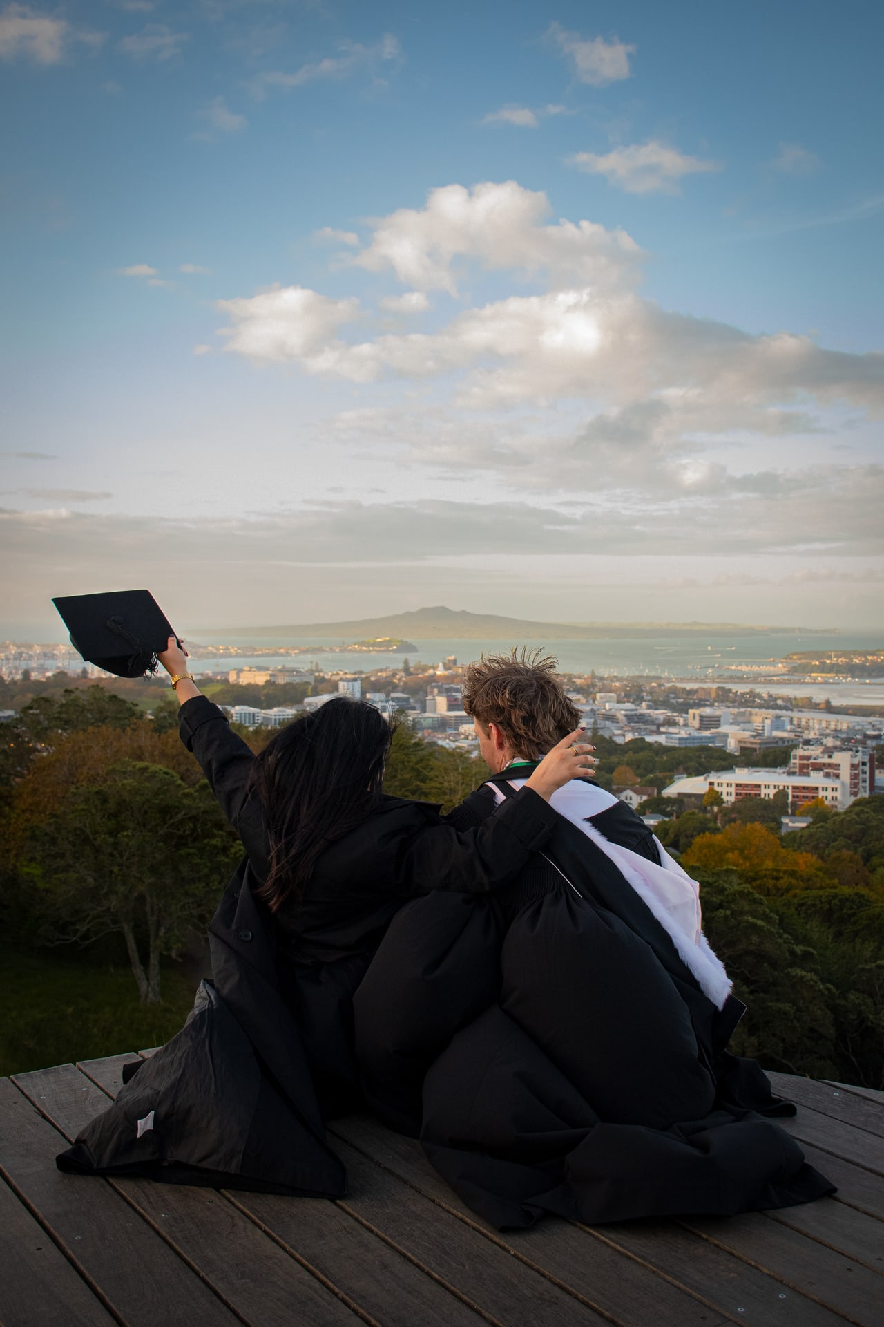 Two graduates on a wooden lookout overlooking Auckland and Rangitoto Island
