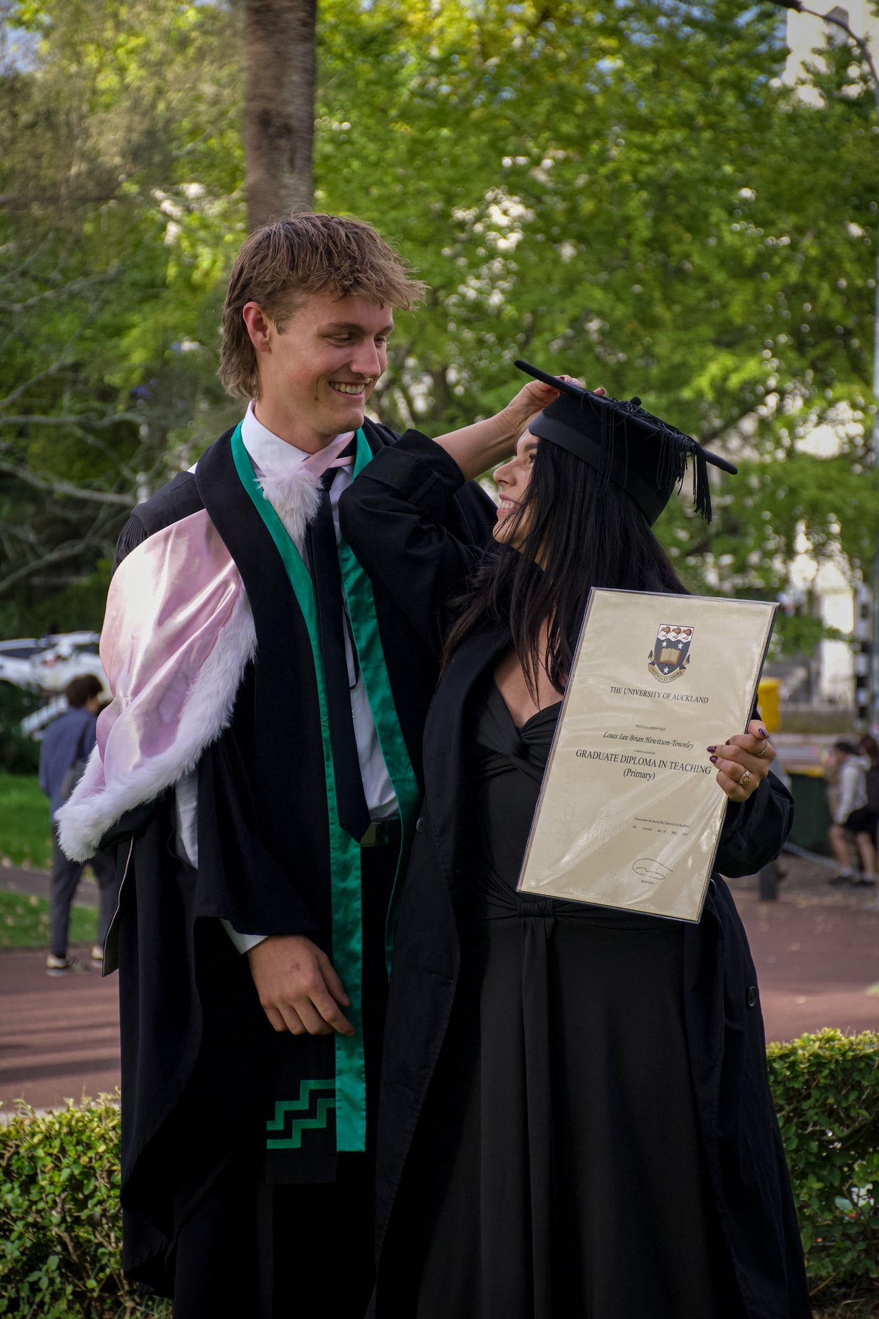 Graduates in academic dress sharing a joyful outdoor moment with a framed diploma